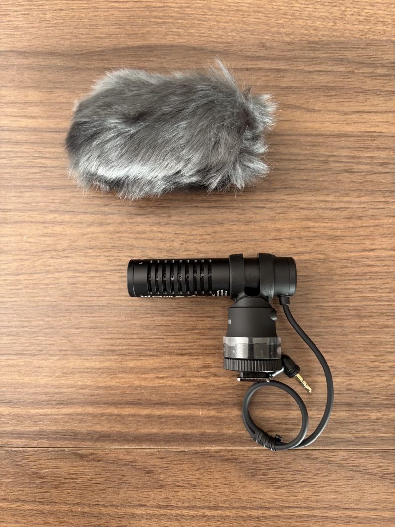 Canon DM-E100 directional stereo microphone lying below its furry wind cover on a wooden desk
