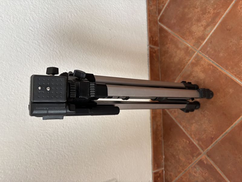 A second, lighter tripod, folded, lying against a white wall